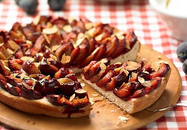 Ein runder Zwetschgenkuchen ist dicht mit Zwetschgenspalten und Mandelblättchen belegt.