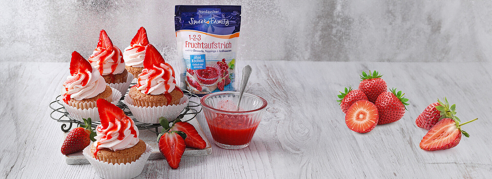 Eine Reihe von Cupcakes mit rotem Fruchtaufstrich und eine Packung 1‑2‑3 Fruchtaufstrich stehen auf einem Brett.