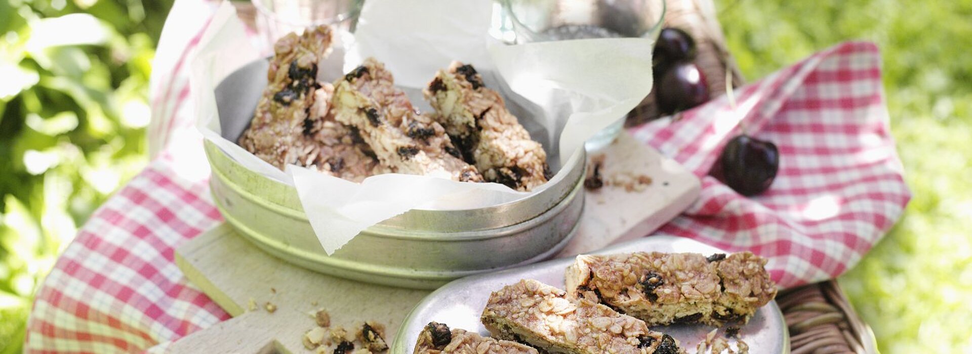 Müsliriegel liegen in silbernen Brotboxen auf einer roten Picknickdecke