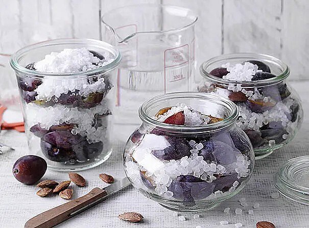 Mehrere Einmachgläser sind mit halbierten Pflaumen und Zucker gefül