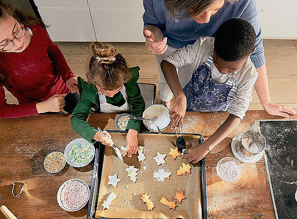 Eine Frau verziert zusammen mit Kindern Kekse gebacken nach dem Rezept von Sweet Family